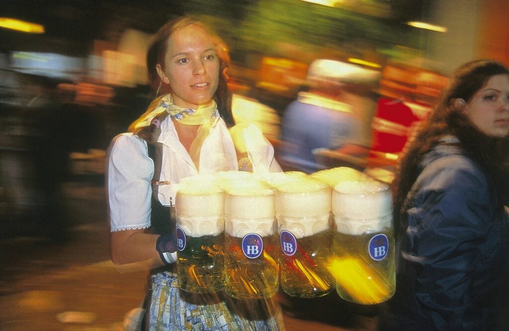 A woman in a dirndl carrying several glass mugs of beer in a hurry.