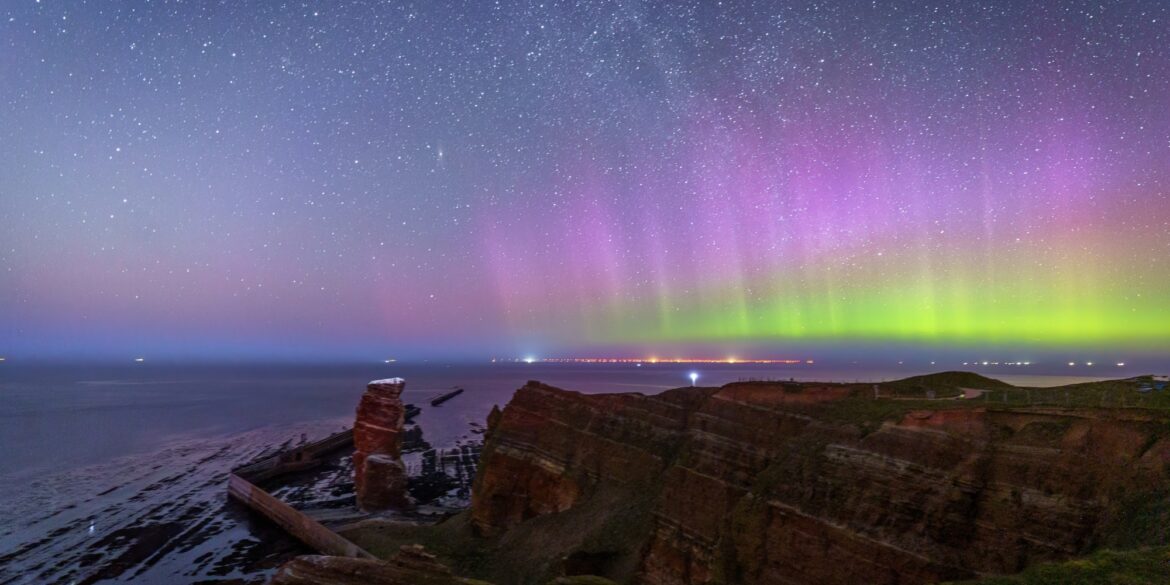 Über den Klippen der Insel Helgoland, links die Lange Anna, scheinen grüne und violette Polarlichter.