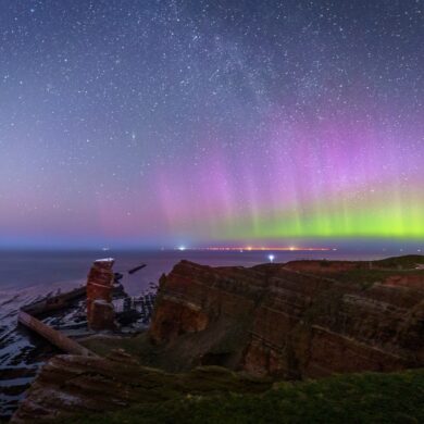 Über den Klippen der Insel Helgoland, links die Lange Anna, scheinen grüne und violette Polarlichter.