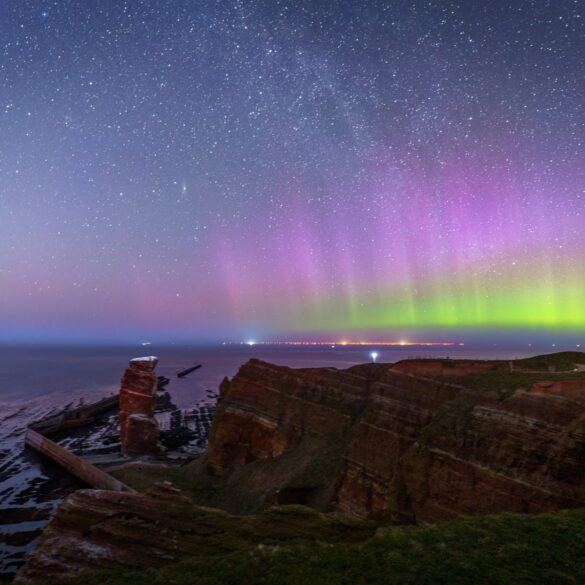 Über den Klippen der Insel Helgoland, links die Lange Anna, scheinen grüne und violette Polarlichter.