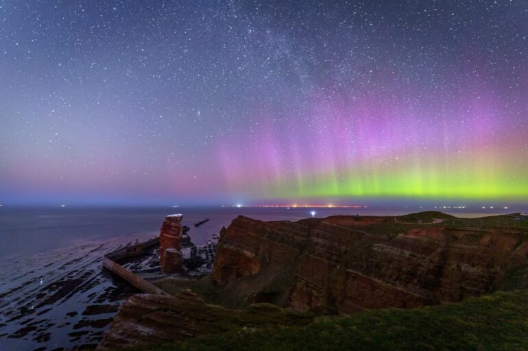 Über den Klippen der Insel Helgoland, links die Lange Anna, scheinen grüne und violette Polarlichter.