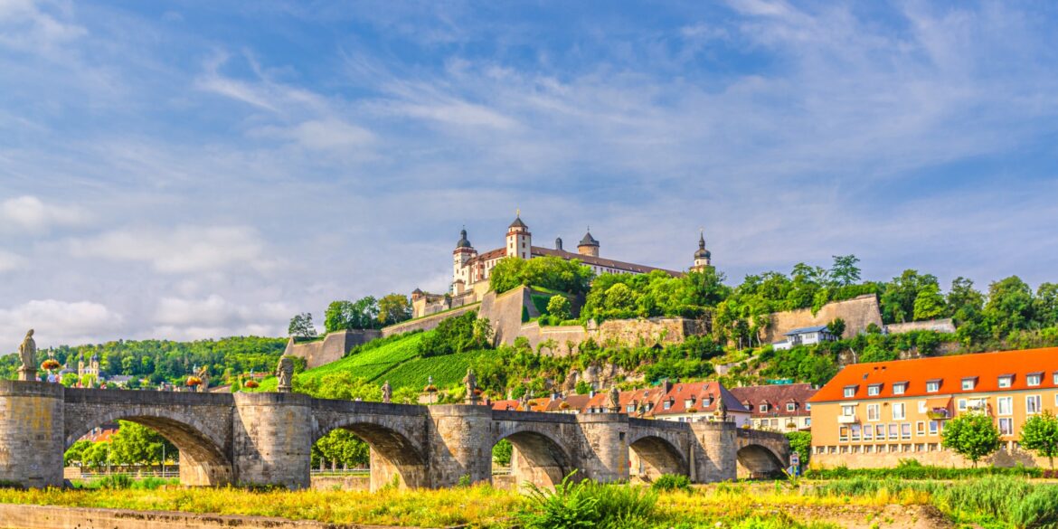 Blick über den Main in Würzburg, mittig eine Brücke, hoch oben auf der anderen Uferseite die mächige Festung der Stadt