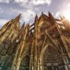 Außenansicht des Kölner Doms, hinter dessen Dach die Sonne hervorscheint.
