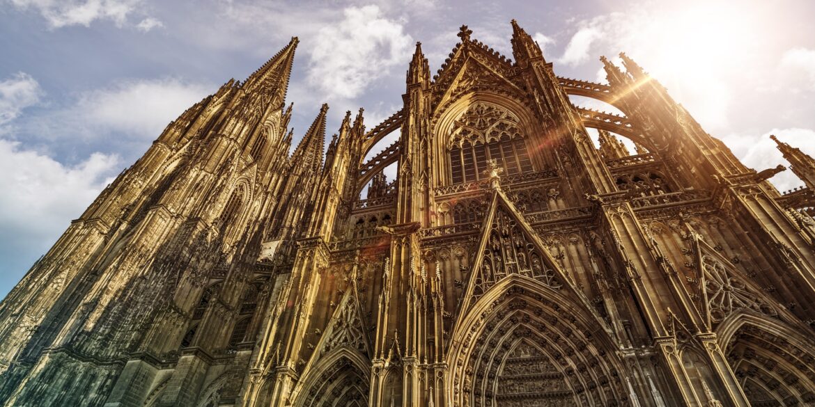 Außenansicht des Kölner Doms, hinter dessen Dach die Sonne hervorscheint.
