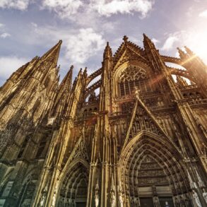 Außenansicht des Kölner Doms, hinter dessen Dach die Sonne hervorscheint.