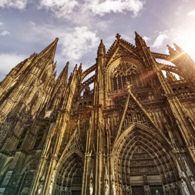 Außenansicht des Kölner Doms, hinter dessen Dach die Sonne hervorscheint.