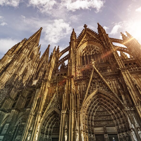 Außenansicht des Kölner Doms, hinter dessen Dach die Sonne hervorscheint.