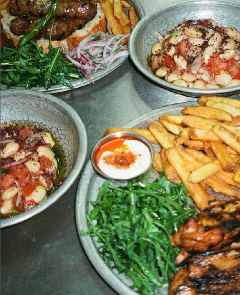 Auf einem Tisch stehen mehrere Teller mit türkischen Gerichten, unter anderem eine große Protion Köfte mit Pommes und Cacik.