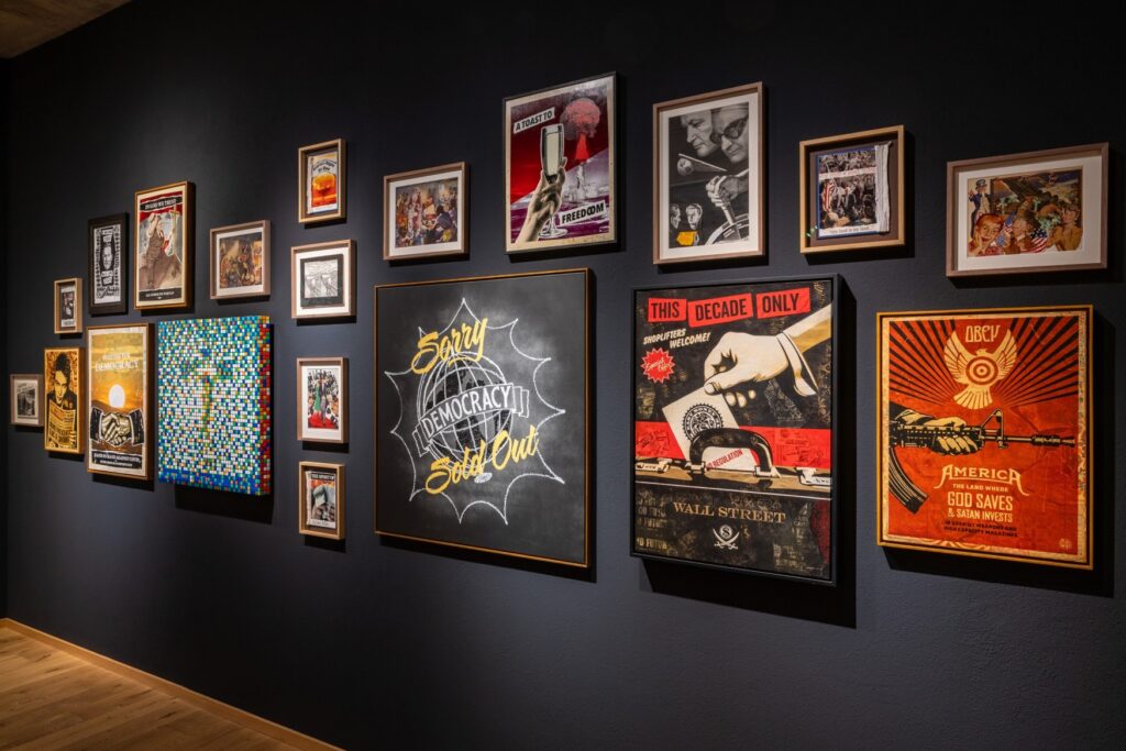 There are many framed posters hanging on a black wall in a museum.