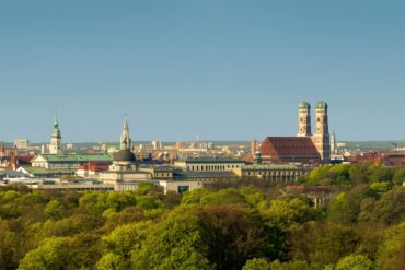 A view over the rooftops of Munich, dotted with green trees and bathed in the soft light of the setting spring sun.