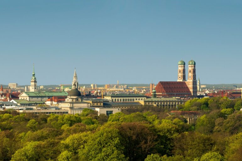 A view over the rooftops of Munich, dotted with green trees and bathed in the soft light of the setting spring sun.