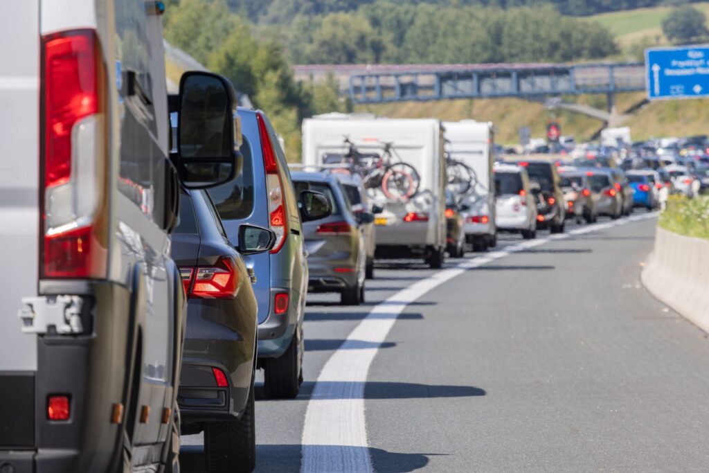 Many vehicles, including several RVs, are stuck in a traffic jam on the highway. The air shimmers with heat above the asphalt.