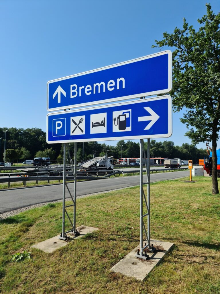 A sign at a highway rest stop points straight ahead to Bremen and to the right toward the parking lot, the gas station, and the food courts.