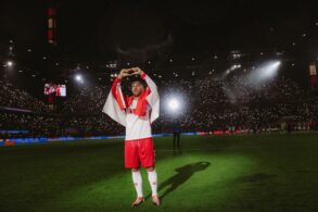 Lukas Podolski stands in the spotlight at the RheinEnergieStadion wearing the 1. FC Köln jersey and forms a heart with his hands.