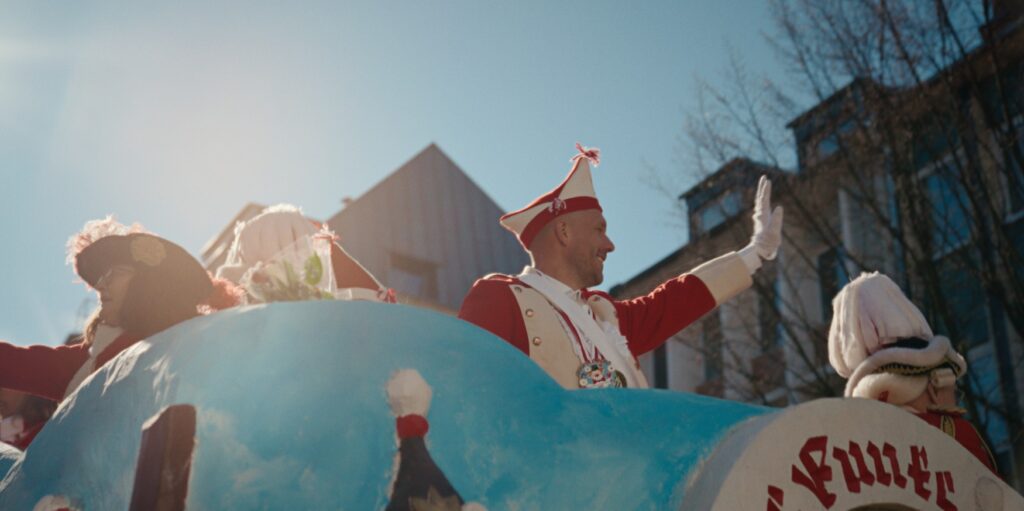 Ein Still aus der Netflix-Dokumentation "Poldi" zeigt Lukas Podolski in Karnevalsgarde-Uniform auf einem Umzugswagen in Köln.