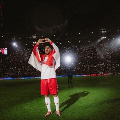 Lukas Podolski steht im Trikot des 1. FC Köln im RheinEnergieStadion im Scheinwerferlicht und formt ein Herz mit den Händen.