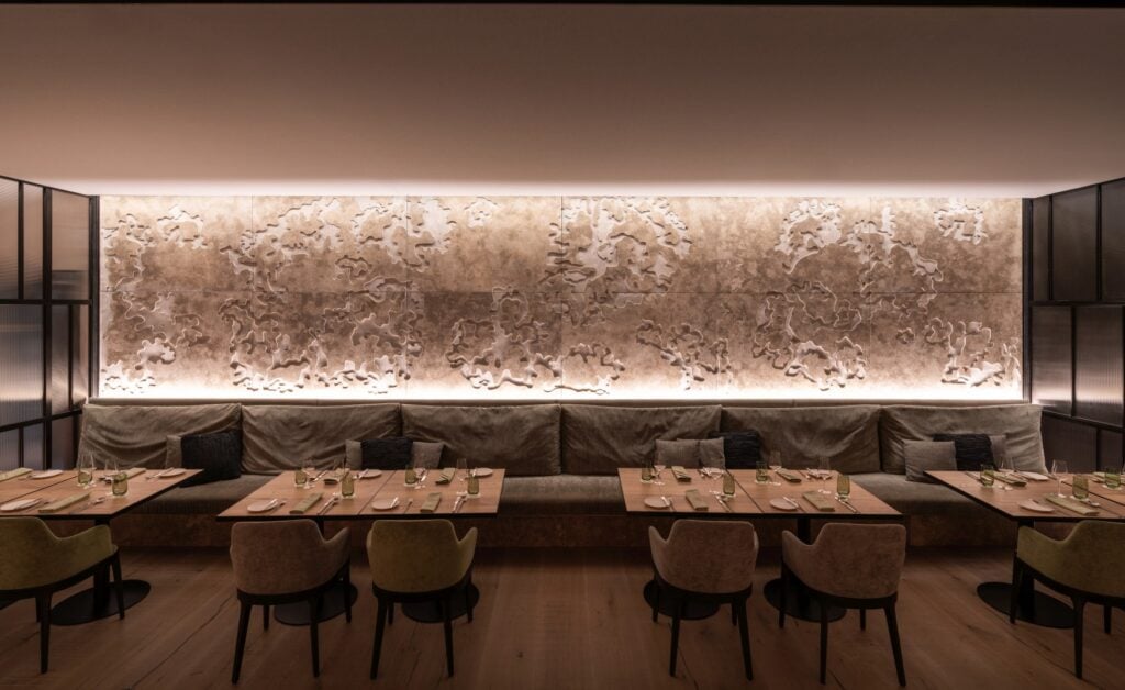 Mehrere Tische im modern eingerichteten Restaurant "Staderer" im Hotel "Das Altmühltal" in Eichstätt. Hinter den Tischen hängt ein modernes Kunstwerk aus Granit an der Wand und wird angeleuchtet.