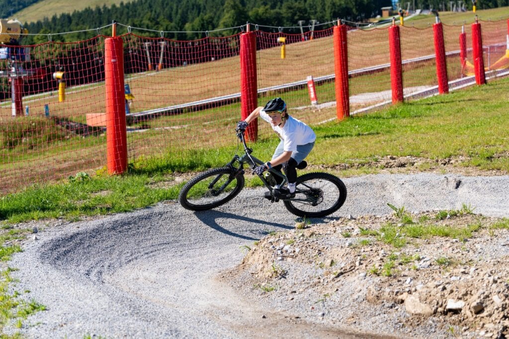 Ein Kind mit Fahrradhelm fährt eine schäg angelegte Kurve mit einem Mountainbike in einem Bikepark.