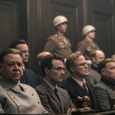 Aufnahme aus dem Film "Nürnberg" (erscheint im Mai). Mehrere Menschen in NS-Uniformen sitzen auf einer Anklagebank, dahinter US-amerikanische Soldaten mit weißen Helmen. Zuvorderst auf der Bank sitzt der Schauspieler Russell Crowe als Hermann Göring, der knapp an der Kamera vorbeischaut.