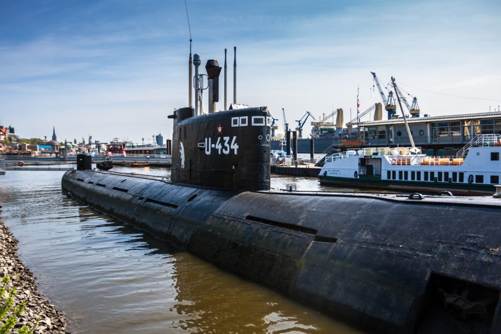 A black submarine marked “U-434” is moored in a harbor basin.