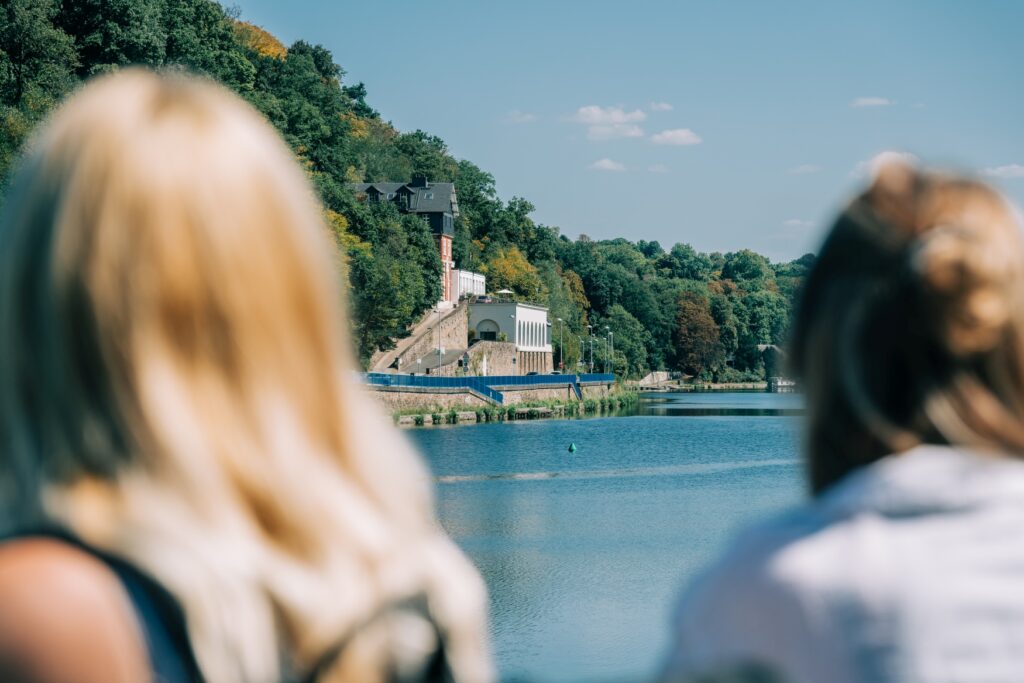 Two people in the foreground, out of focus, are looking at a reservoir and the weir on the shore.