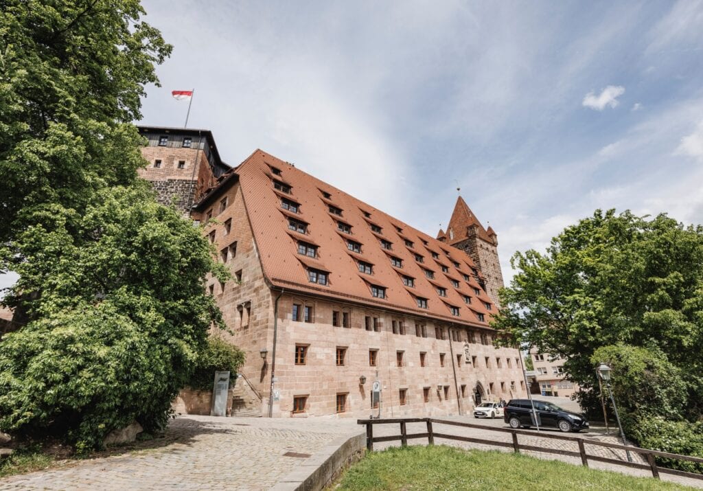 Ein Gebäude der Kaiserburg Nürnberg in markant rotem Sandstein, mit vielen Fenstern in der Wand und auf dem Dach.