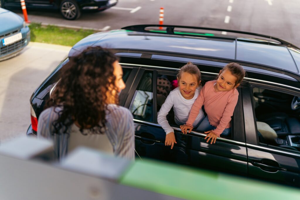 A woman is filling up her car and turns her head toward her two children, who are peering out the car window.
