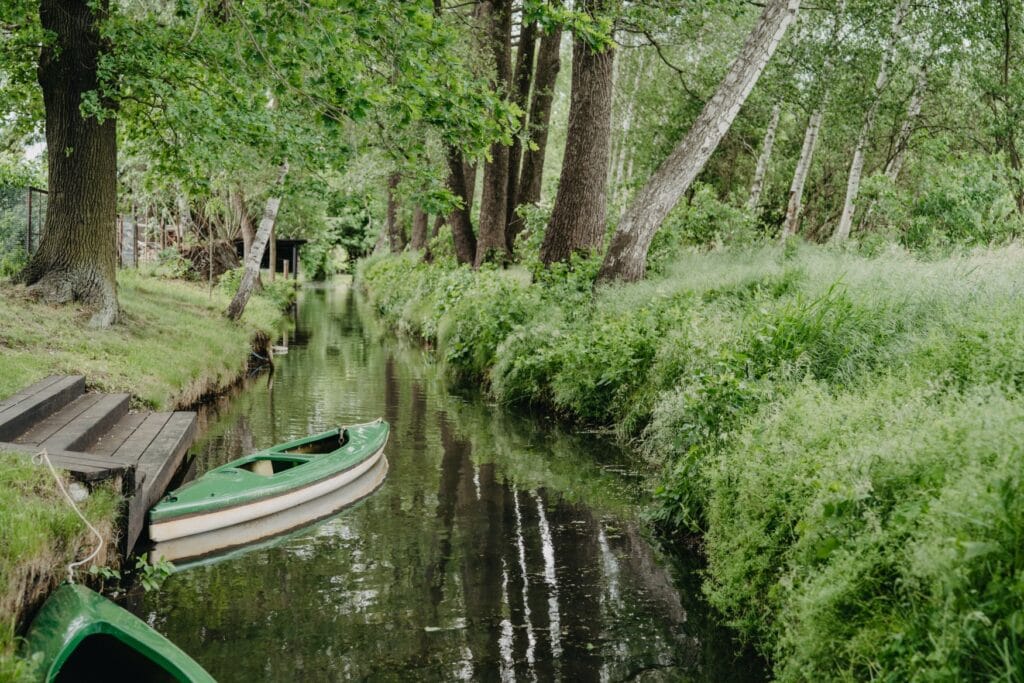 In einer schmalen Fliesse im grünen Spreewald liegt ein Kanu angeleint an einem Anleger.