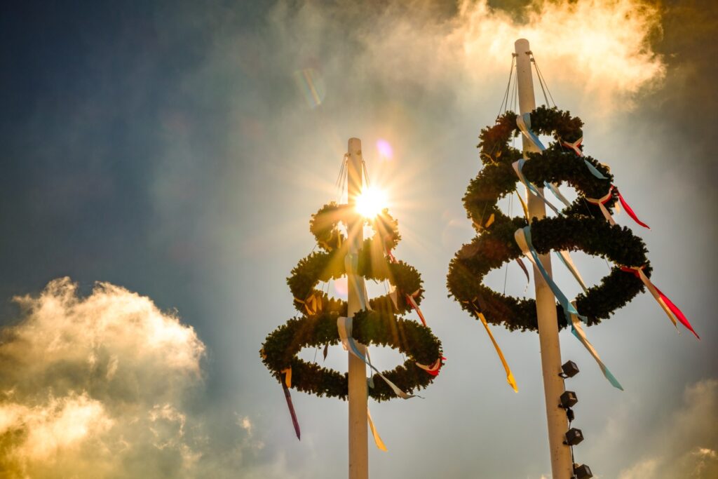 Two elaborately decorated maypoles stretch up into the blue sky.
