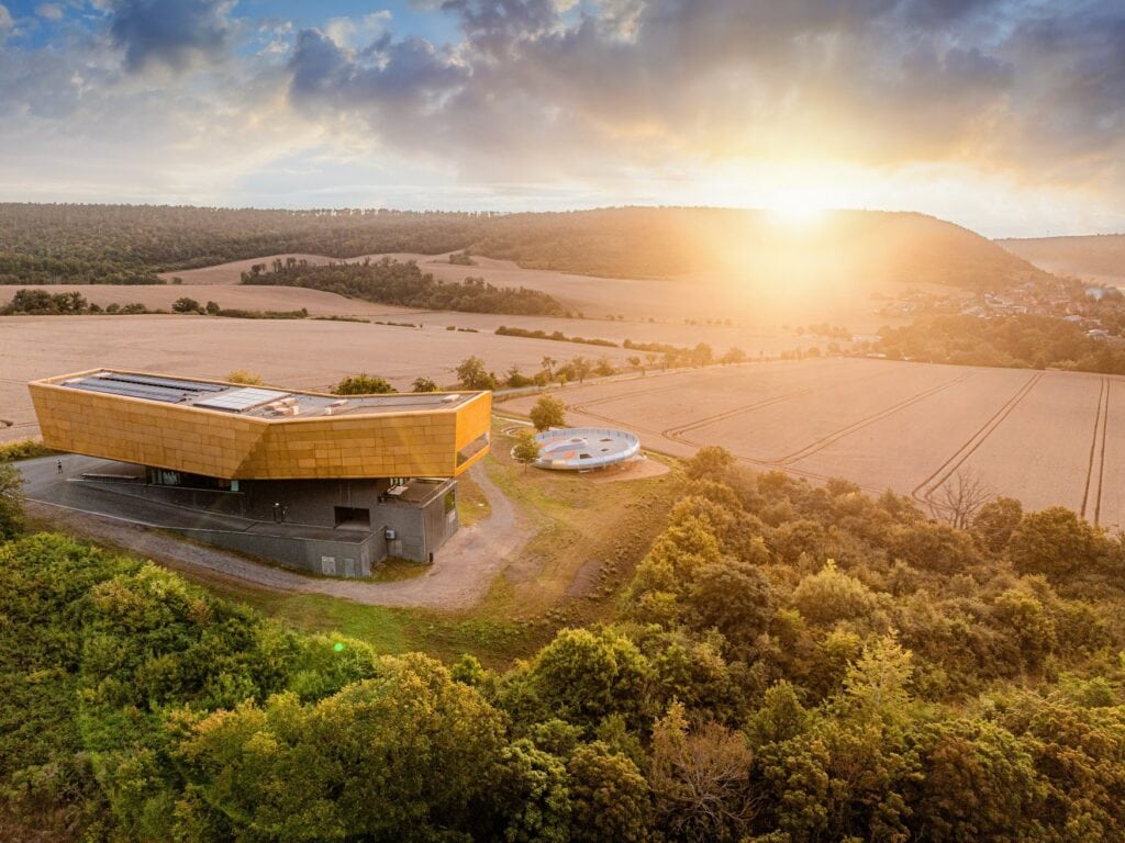 Luftaufnahme der Arche Nebra mit dem goldenen Museumsgebäude und dem runden Freigelände auf dem Mittelberg bei Nebra im Sonnenuntergangslicht.