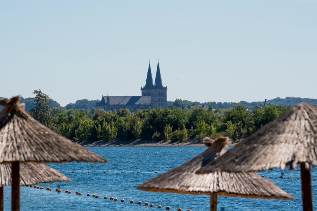 Über einige Strandschirme aus Stroh hinweg geht der Blick über den Xantener Südsee zum Xantener Dom