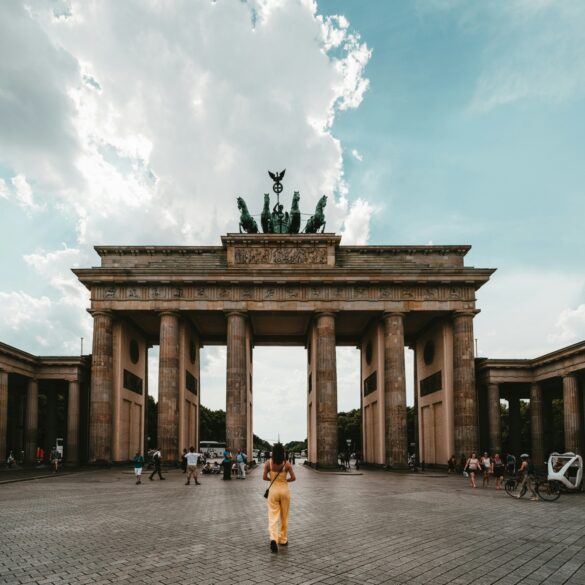 A person wearing a yellow summer dress is standing right in the center in front of the Brandenburg Gate in Berlin.