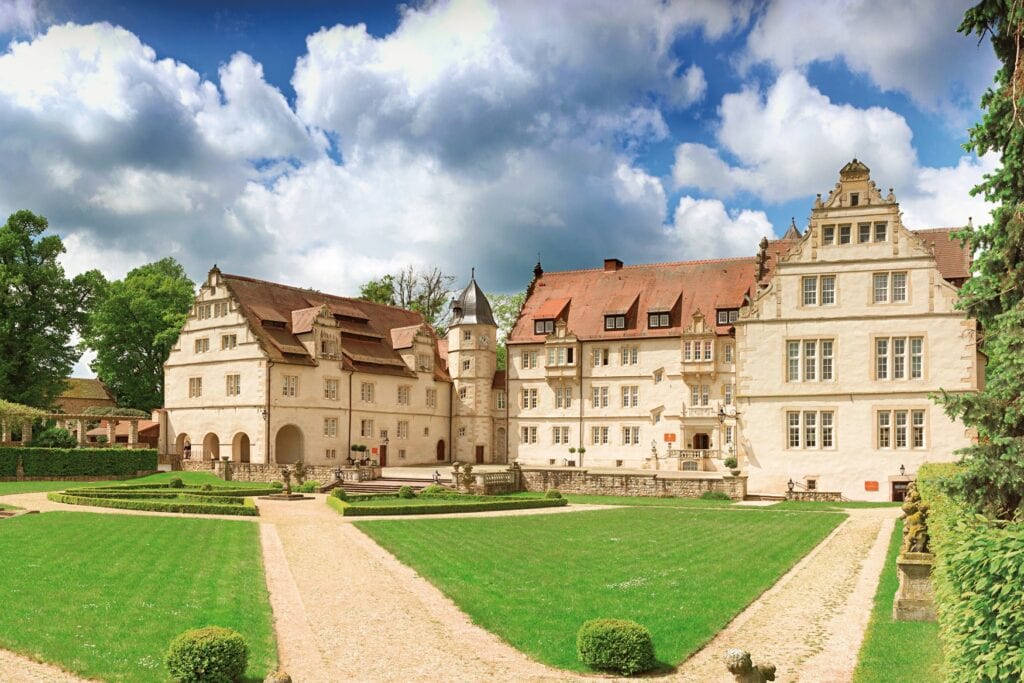 Blick vom Garten auf das dreiflügelige Schloss Schwöbber, mit hell getünchten Wänden und roten Ziegeldächern.