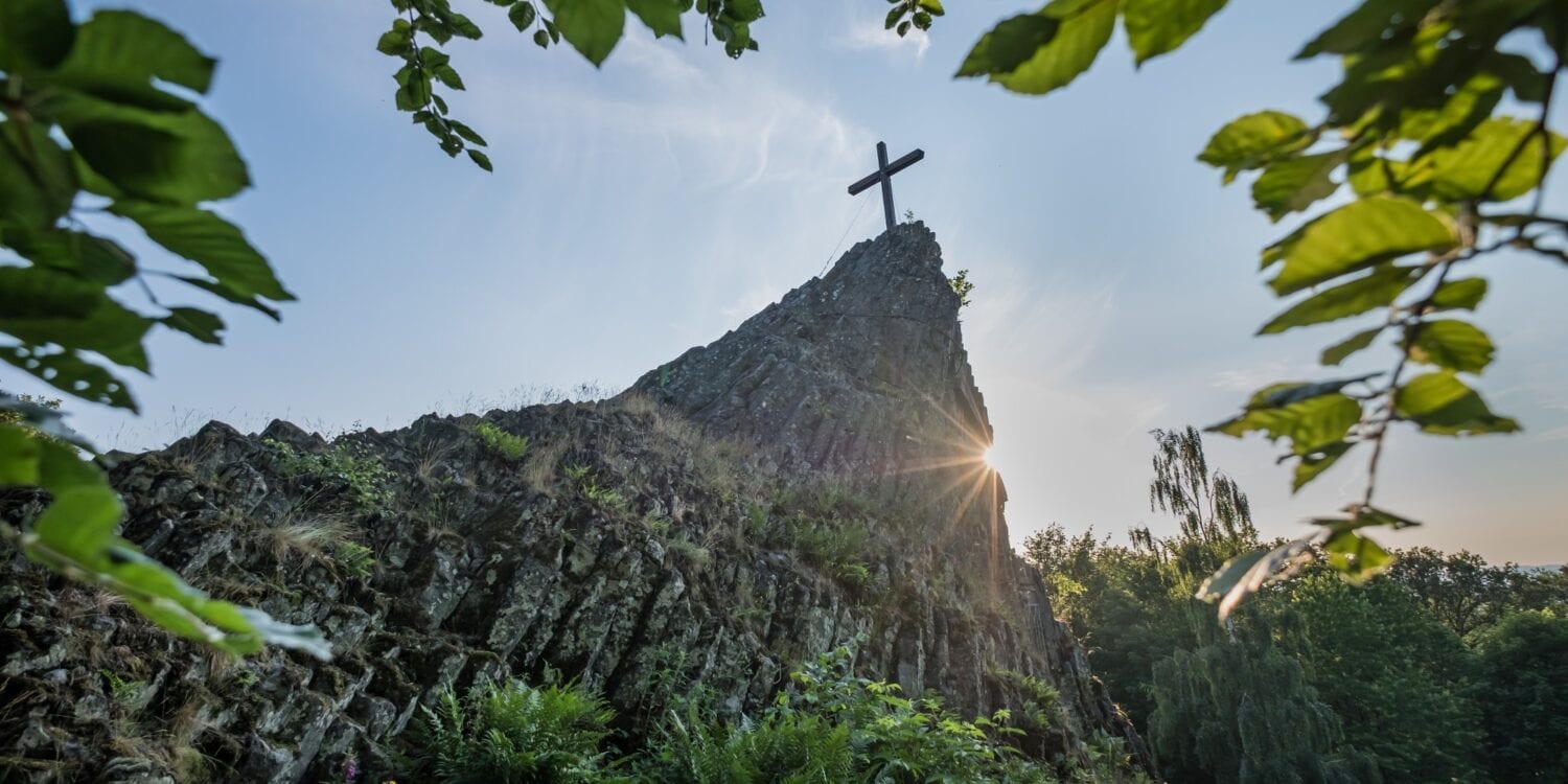 Blick auf den Druidenstein mit Gipfelkreuz, hinter dem sich die Sonne hervorstiehlt.