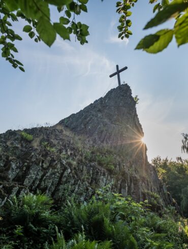 Blick auf den Druidenstein mit Gipfelkreuz, hinter dem sich die Sonne hervorstiehlt.