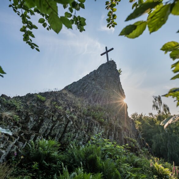 Blick auf den Druidenstein mit Gipfelkreuz, hinter dem sich die Sonne hervorstiehlt.