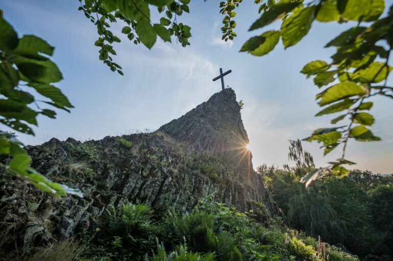 Blick auf den Druidenstein mit Gipfelkreuz, hinter dem sich die Sonne hervorstiehlt.