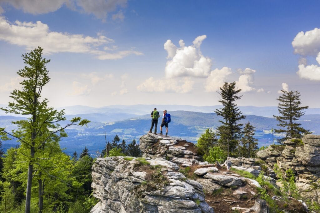 Zwei Wanderer stehen auf einem Felsenvorsprung über dem Bayerischen Wald