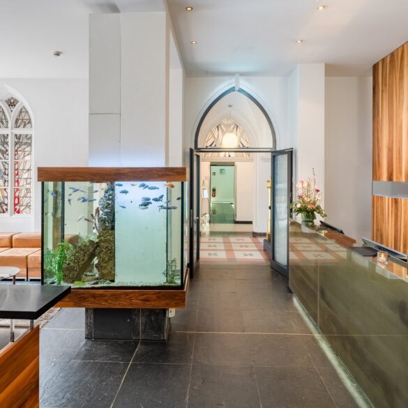by des Hopper Hotels in einer umgebauten Kölner Kirche mit Empfangstresen, großem Aquarium als Raumteiler, gotischen Spitzbogenfenstern und Blick durch den historischen Kirchenbogen.