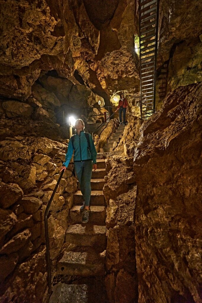Besucher steigt in der Tiefenhöhle Laichingen auf der Schwäbischen Alb eine in den Fels gemeißelte Treppe hinab, während eine zweite Person von oben in die Höhle schaut.