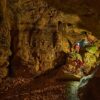Zwei mit Stirnlampen ausgerüstete Personen klettern in der Tiefenhöhle Laichingen auf der Schwäbischen Alb über Felsblöcke durch einen weitläufigen Höhlengang.