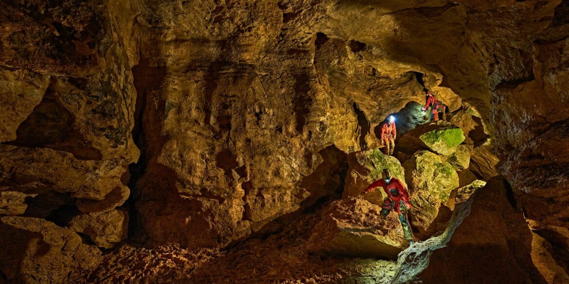 Zwei mit Stirnlampen ausgerüstete Personen klettern in der Tiefenhöhle Laichingen auf der Schwäbischen Alb über Felsblöcke durch einen weitläufigen Höhlengang.