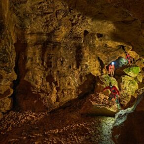 Zwei mit Stirnlampen ausgerüstete Personen klettern in der Tiefenhöhle Laichingen auf der Schwäbischen Alb über Felsblöcke durch einen weitläufigen Höhlengang.