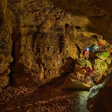 Zwei mit Stirnlampen ausgerüstete Personen klettern in der Tiefenhöhle Laichingen auf der Schwäbischen Alb über Felsblöcke durch einen weitläufigen Höhlengang.