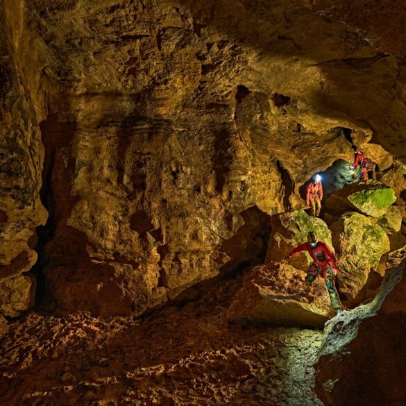 Zwei mit Stirnlampen ausgerüstete Personen klettern in der Tiefenhöhle Laichingen auf der Schwäbischen Alb über Felsblöcke durch einen weitläufigen Höhlengang.