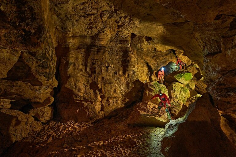Zwei mit Stirnlampen ausgerüstete Personen klettern in der Tiefenhöhle Laichingen auf der Schwäbischen Alb über Felsblöcke durch einen weitläufigen Höhlengang.