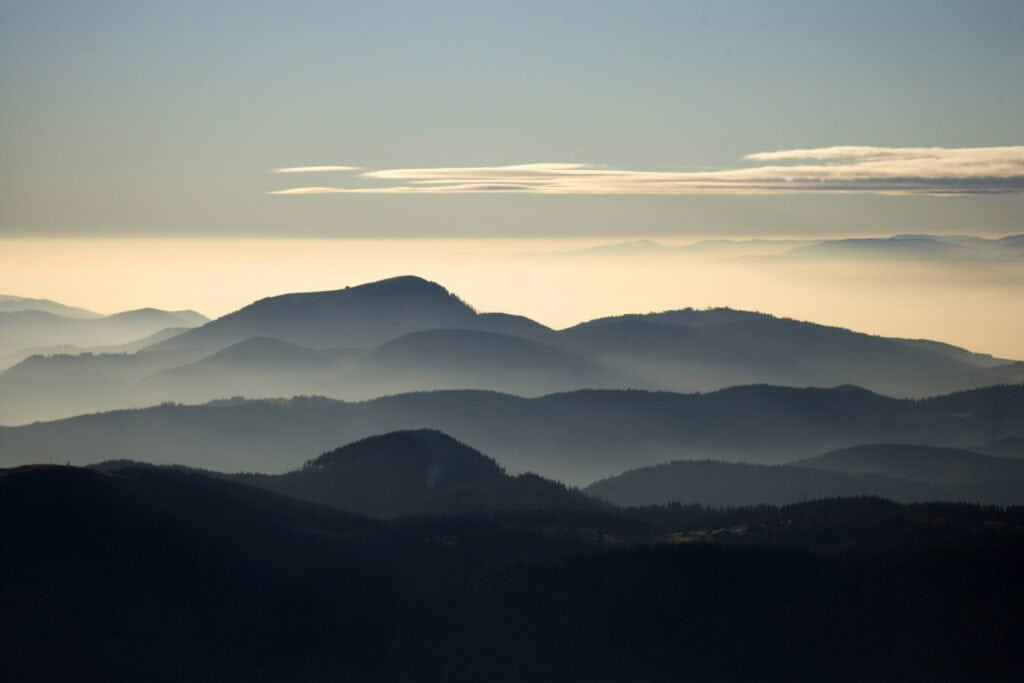 Gestaffelte Bergrücken des Schwarzwalds zeichnen sich im Dunst hintereinander ab. Über dem Horizont färbt sich der Himmel im warmen Licht des frühen Abends.