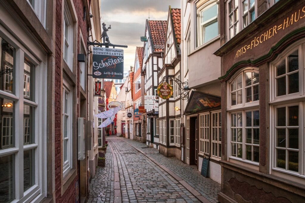 Narrow cobblestone lane in Bremen's Schnoor quarter with half-timbered houses, hanging shop signs and the Amtsfischerhaus.