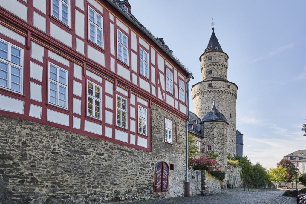 Blick in Idstein im Taunus auf ein rot-weißes Fachwerkhaus und den runden steinernen Hexenturm mit spitzem Dach dahinter.