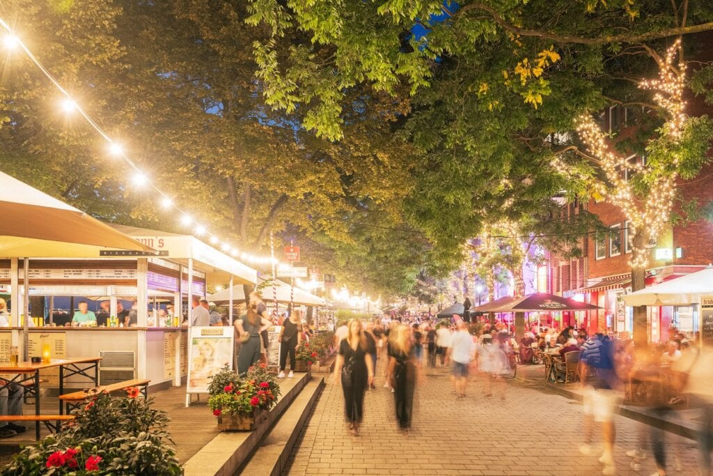 Bremen's Schlachte promenade at night, with string lights in the trees, beer garden stands and people walking along the riverside.